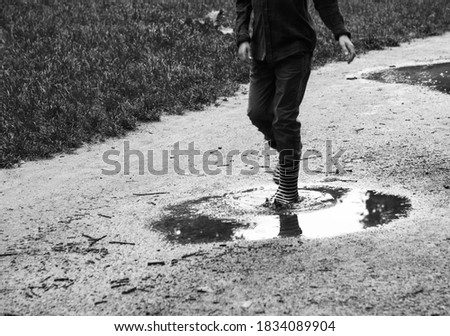 Childhood fun days nostalgia memories. Boy in striped rain boots walking through puddles in forest. Simple life joy, healthy natural lifestyle concepts. Black white old times historic photo.