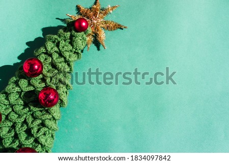 Handmade knitted Christmas tree with a Golden tinsel star on the top of the head and red shiny balls on a light green background. Beautiful minimalistic Christmas background.