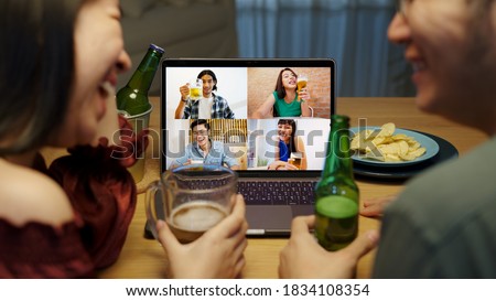 Young happy asian couple enjoy relax night party event online celebration festive with friends at home clinking beer with glass and bottle toasting drinking via video call. Royalty-Free Stock Photo #1834108354
