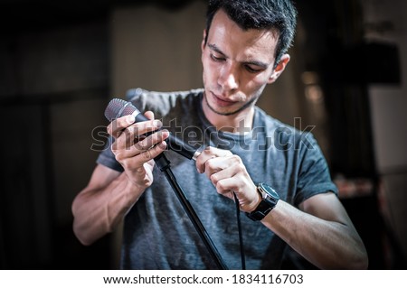 Theater audio technician adjusting an microphones on the scene. Installing and testing the sound system in the background