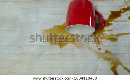 A picture of a coffee drink spilled out of a red glass on a white wood floor