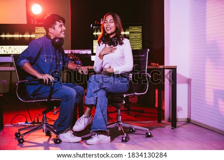 Pretty Asian female tries to sing with her producer in the studio in a rehearsal session. Performance and show in the music business. Image with copy space. Small and home recording studio.