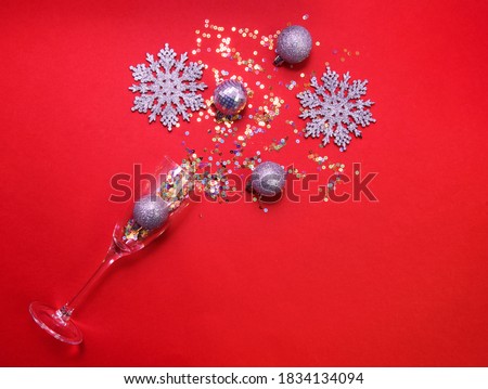 Glass of champagne with silver balls, sparcles confetti and glitter snowflakes on the red background.