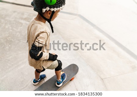 Young boy wearing safety gear at the skateboard park, back view