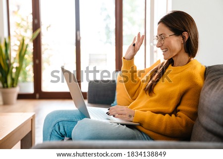 Beautiful caucasian pleased woman smiling and using laptop while sitting on sofa in apartment