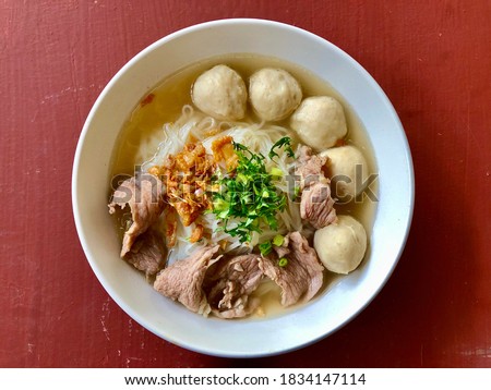 Top view of a white bowl of Thai pork noodle with ,braised pork, sliced pork,meatball,on wooden table.Noodles are fast food.Thai food noodle.Thai street food market.