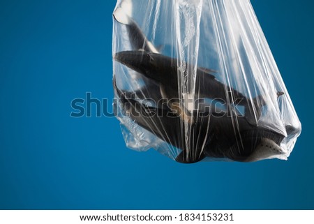 Ocean pollution concept, toy whales in plastic bag on blue background