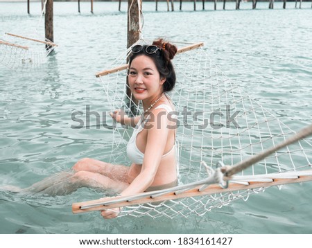 asian pregnant woman in bikini sitting on hammock in turquoise sea water near beach. tropical beach in Koh Kut Island, Thailand. pregnancy relaxation concept.