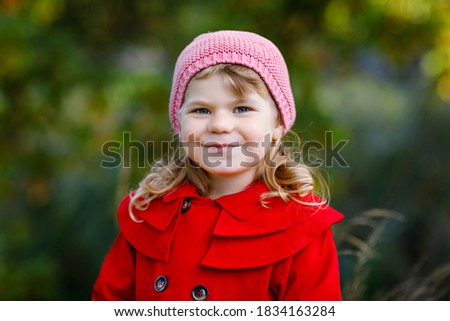 Cute little toddler girl in red coat making a walk through autumn forest. Happy healthy baby enjoying walking with parents. Sunny fall day with child. Active leisure and activity with kids in nature