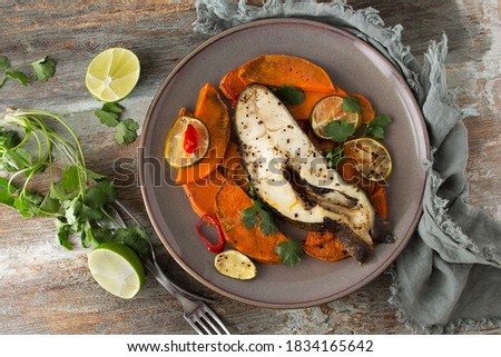flat lay of plate of baked halibut steak with lime, chili and sweet potato on wooden table