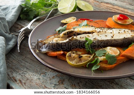 plate of baked halibut steak with lime, chili and sweet potato on a wooden table
