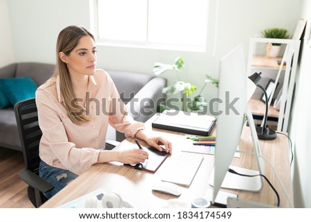 Portrait of a busy female illustrator doing some work in her office with a graphic tablet and a computer