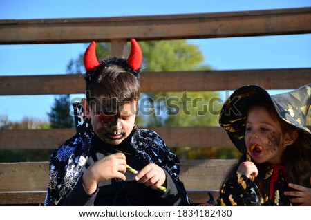 children in halloween costumes on holiday a girl in a witch suit a black hat on the head with black Halloween make-up, boy in devil halloween costume with horns zombie eating sweets jelly worms