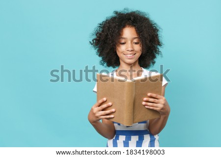 Pretty little african american kid girl 12-13 years old in striped clothes isolated on pastel blue wall background studio portrait. Childhood lifestyle concept. Mock up copy space. Reading book Royalty-Free Stock Photo #1834198003