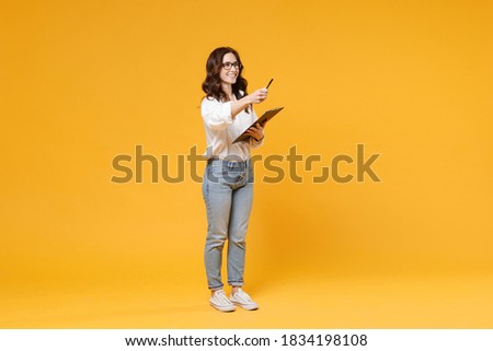 Smiling young business woman in white shirt glasses isolated on yellow background. Achievement career wealth business concept. Mock up copy space. Hold clipboard with papers document, point pen aside