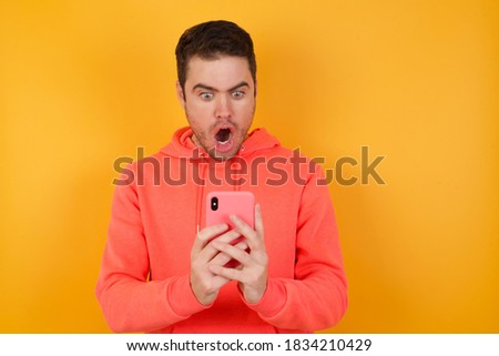Focused Handsome man with sweatshirt over isolated yellow background use smartphone reading social media news, or important e-mail 