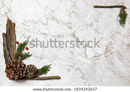Christmas background.Pinophyta, brown pinecone with tree leaves, gift and red fruits on white marble.
