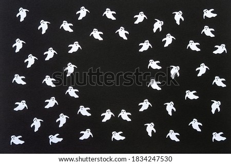 Halloween background. White confetti ghosts on black paper background. Happy Halloween concept. Greeting card, festive backdrop for Halloween holiday. Flat lay, top view, copy space