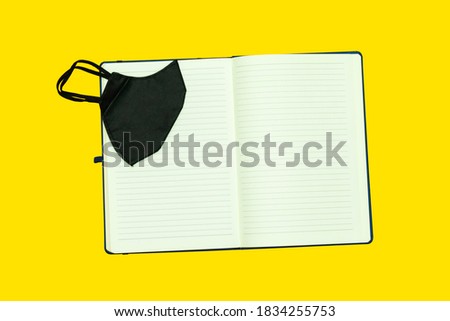 agenda book or notebook with black mask isolated on yellow background