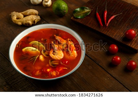 Tom yam soup with shrimp and lime in a light bowl next to lime, pepper chili and cherry.