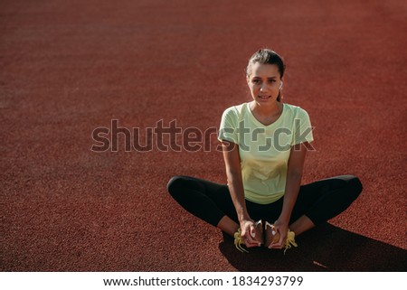 Strong dark-haired woman in trendy sport outfit doing exercises for legs at local stadium. Happy female leading healthy and active lifestyle.