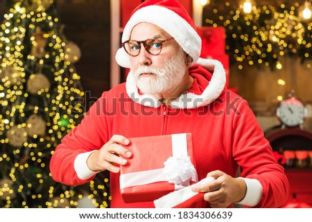 Funny Santa hold Christmas gift. Santa wishes merry Christmas. Santa grandfather with a white beard posing on the Christmas wooden background