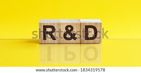r and d word written on wood block. r and d word is made of wooden building blocks lying on the yellow table. sales, business concept, yellow background