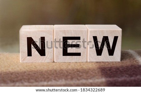 The word NEW is written on wooden cubes. Wooden cubes in the open air, overlooking the countryside. For business related design. Marketing concept.