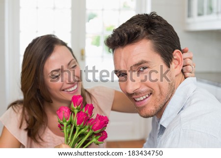 Cheerful young woman looking at man with flowers at home