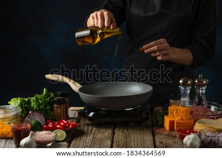 Professional chef pours oil into pan wok with ingredients for tacos background. Backstage of preparing traditional mexican tacos. Concept of tasty street food. Dark surface.