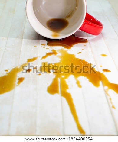 A picture of a coffee drink spilled out of a red glass on a white wood floor