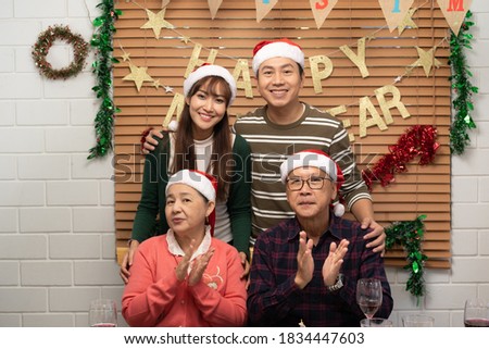 Happy Asian family, father mother and grandparent making family photohoot together at dinner table with Happy New Year banner as the background during Xmas dinner in a Xmas decorated dining room. 