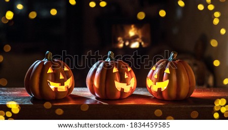 Three cheerful glowing Halloween pumpkins stand on a wooden table on a dark background.