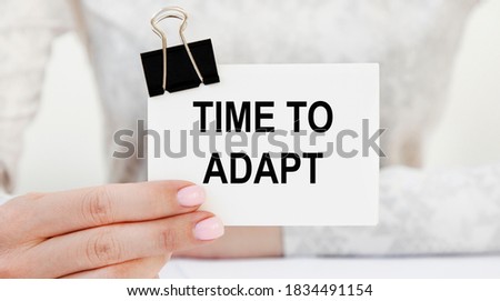The girl holds a card with the text TIME TO ADAPT.