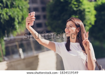 Photo portrait of girl making v-sign taking selfie with phone outdoors