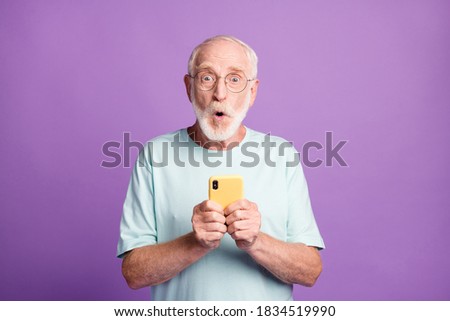 Photo portrait of shocked old man holding phone in two hands isolated on vivid violet colored background