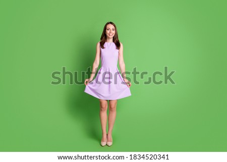 Full size photo of pretty adorable young slim girl lady look camera two arms hold bottom dress advert artistic school clothes brand wear purple outfit isolated pastel green color background