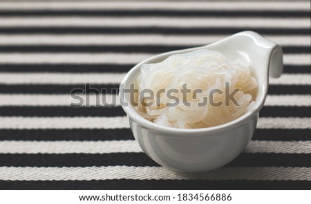 Front view  of Konjac or Shirataki noodles in white bowl  on black and white stripe table cloth background.