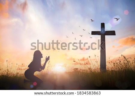 Silhouette woman hand rising for worship God over cross on sunset background
