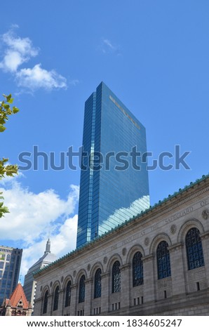 Street view of the John Hancock Tower in Boston with old gothic building in the foreground and some skyscrapers in the background with blue sky