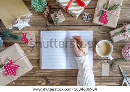 Desktop mock up planner. Flat lay of Woman s hands writes in a notebook and wrapping Christmas gift. Presents on wooden background with decor elements, top view. New year packing Concept, top view