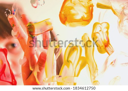 Beautiful young girl painting artwork on glass with colorful hands and finger. Happy childhood, art, painting lessons concept. Selective focus on finger. 