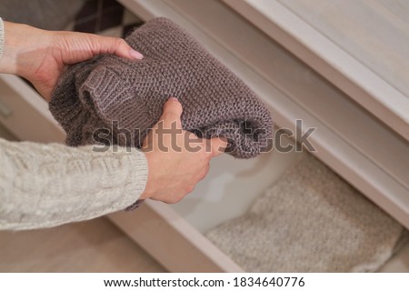 Women's hands put winter clothes in a drawer of a wooden chest of drawers, the concept of warmth and comfort, order in the storage of things, winter cold