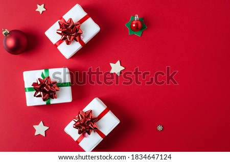 Gifts packed in white paper tied with red and green ribbons lie on a bright red vertical background with copy space