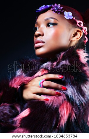 young pretty african american woman in spotted fur coat and flowers jewelry posing on black background