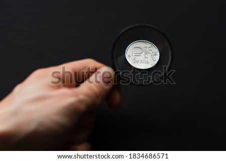 Ruble coin viewed through magnifying glass on black background. First person view. Investment in Russian economy. Search for investment decisions
