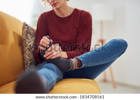 Woman with feet intense pain sitting on a couch at home.