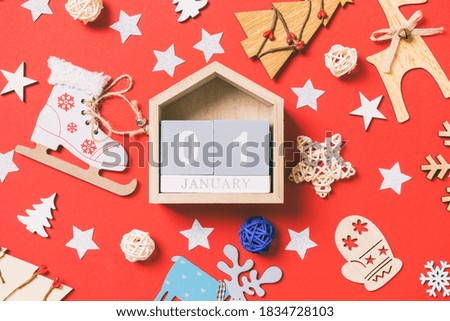 Top view of wooden calendar, holiday toys and decorations on red Christmas background. The first of January. New Year time concept.