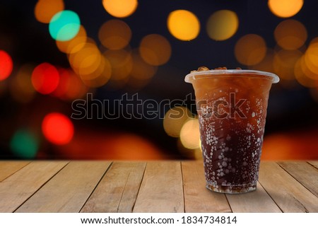 Black soft drinks in plastic glasses (Aeration beverage) placed on a plank floor. Bokeh background illuminated celebration.