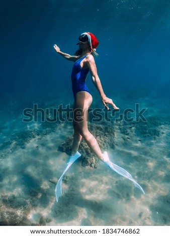 Happy freediver girl with New year cap glides underwater in blue ocean. Christmas holidays concept